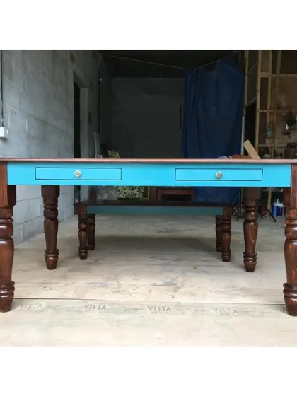 This large dining or work table features a colorful apron with drawers for storage, supported by robust turned legs.