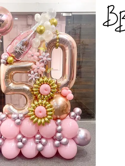 Cheers to 50 years with this pink champagne-themed arrangement. The rose gold '50' is paired with a popping champagne bottle balloon and intricate gold and pink balloon flowers, creating a celebratory and elegant display.