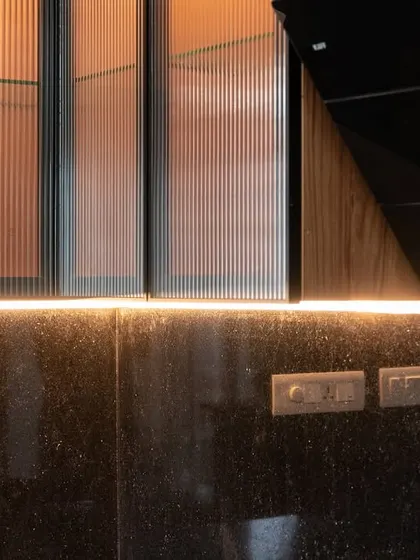 A detail shot of under-cabinet LED strip lighting over a black granite countertop. This highlights the fluted glass on the upper cabinets and provides excellent task lighting.