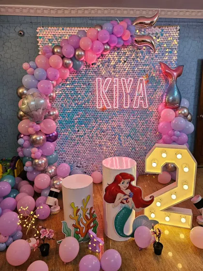 An underwater fantasy with this Little Mermaid theme for a 2nd birthday. The iridescent sequin wall mimics shimmering water, complemented by a pink and purple balloon arch and an Ariel cutout.