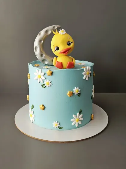 A cute duckling cake that is sure to make you smile. This cake features a hand-sculpted fondant duckling sitting on a moon, surrounded by daisies. It's almost too cute to eat!