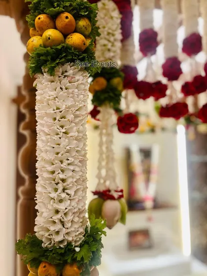 A close-up of a traditional floral pillar combining white 'sugandharaja' flowers with fruits. We cover techniques for creating unique and auspicious decor elements for poojas and weddings.