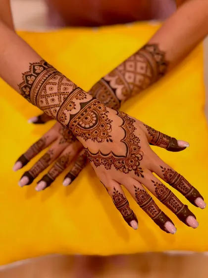 A crossed-hands view of the engagement mehendi against a bright yellow background.
