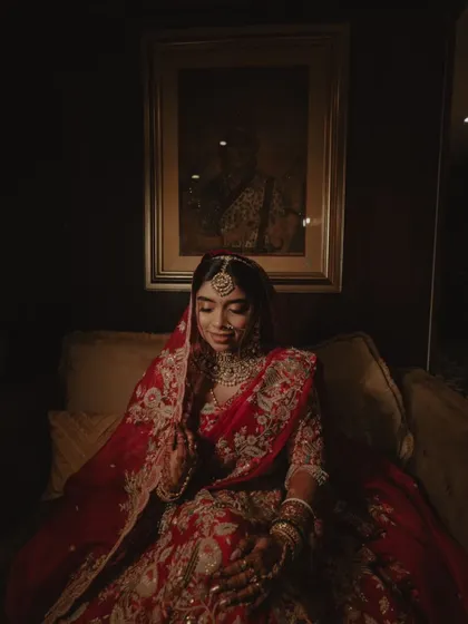 A classic bridal portrait, with the bride seated in a dimly lit, elegant room. The warm lighting creates a vintage, painterly feel.