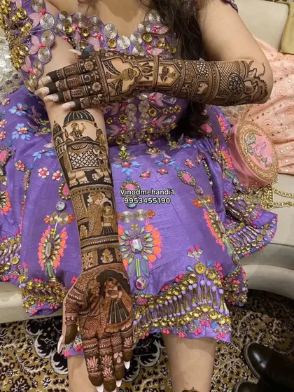 A bride poses with her elaborate story mehendi, which includes a groom's procession, a bride's portrait, and a doli scene, all in one continuous design.
