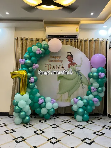 A charming Princess Tiana theme for a first birthday. The decoration features a custom backdrop of the Disney princess, framed by a beautiful balloon arrangement in shades of green and lilac.