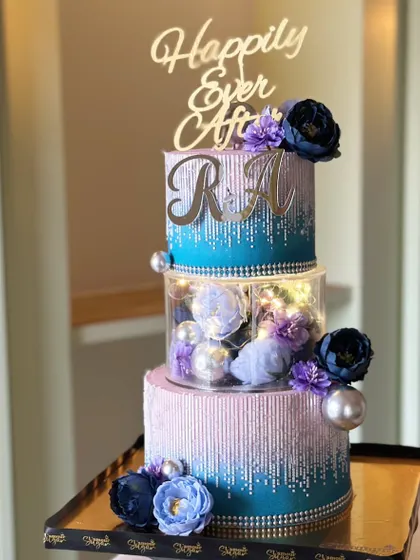 Love baked in hues of blue and purple. This dreamy three-tier cake features a sparkling drip effect and a clear center tier filled with beautiful flowers, perfect for a modern couple.