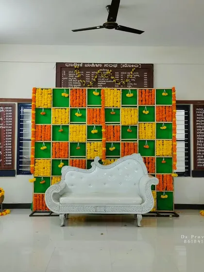 A vibrant and traditional backdrop perfect for a Haldi or baby shower ceremony. This setup uses a checkerboard pattern of green cloth with orange and yellow marigold flower strings.