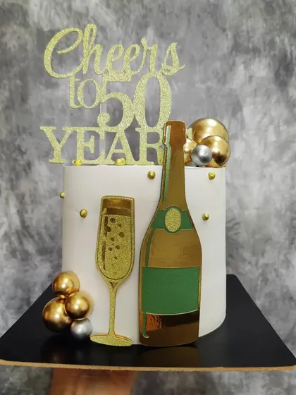 A "Cheers to 50 Years" cake. This design features a gold glitter champagne bottle and glass for a festive 50th birthday or anniversary.