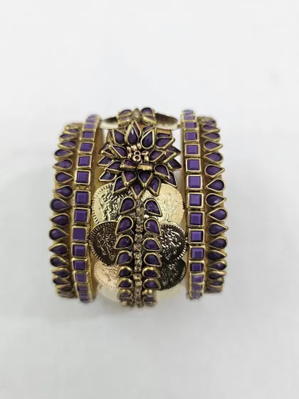 This unique purple and gold bangle set combines silk thread with oxidised coins and a central floral kundan piece. It's a statement design for brides who want something bold and traditional.