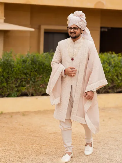 The groom, Hanshul, looking dapper in his classic ivory sherwani with an elegant drape, a perfect example of timeless royal style.