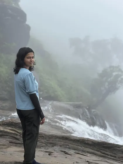 A trekker looks over her shoulder at the misty drop of Bandaje Falls.