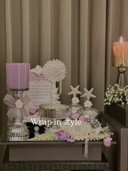 This elegant lilac-themed hamper is perfect for any celebration. It includes a scented candle, a decorative photo frame, and other beautiful items, all arranged on a mirrored tray with delicate flowers.