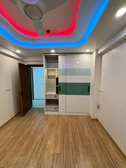 A bedroom with a unique ceiling design featuring multi-colored LED strip lights. The sliding wardrobe with a green and white pattern adds a playful and modern touch to the room.