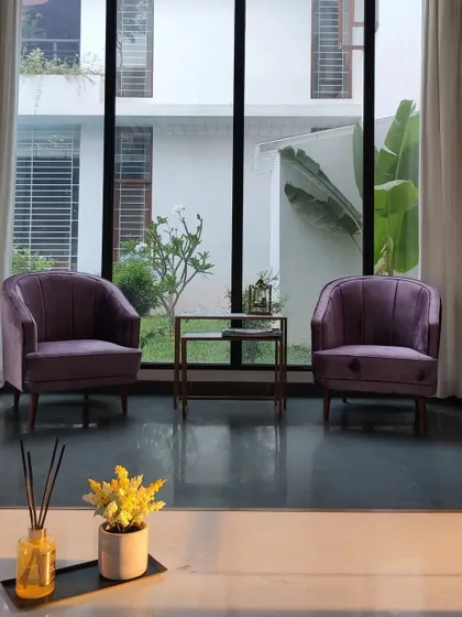 A pair of elegant purple armchairs are perfectly positioned to enjoy the view of the garden through the large, floor-to-ceiling windows.