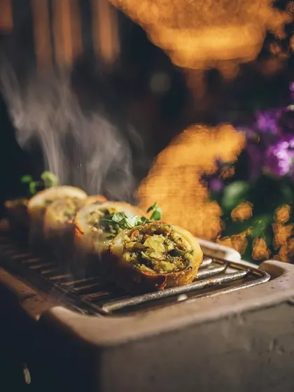 A close-up of smoking appetizers on a mini grill, with a beautiful floral background.