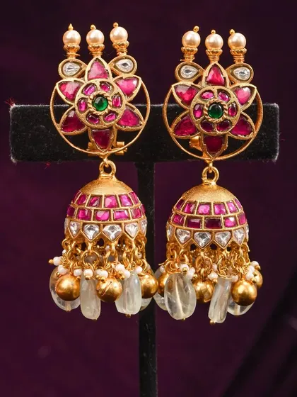 Exquisite handcrafted jhumkas with a floral stud made of kundan-style pink stones. The bell is also decorated with pink stones and finished with clusters of clear and pearl beads.