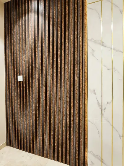 A close-up of a feature wall combining two distinct textures: dark, fluted wood paneling and white marble with elegant gold inlay. This juxtaposition creates a sophisticated and modern look.