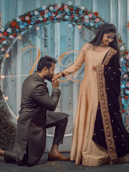 A groom-to-be kneels and kisses his partner's hand during their engagement ceremony. This classic, romantic gesture is beautifully captured against a floral backdrop.