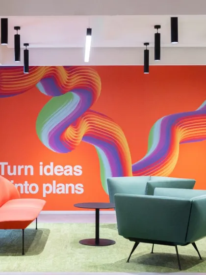 A vibrant wall graphic with the motto "Turn ideas into plans" creates an inspiring backdrop for this informal meeting area. The colorful, flowing artwork and modern furniture combine to foster a creative and forward-thinking atmosphere in the workplace.