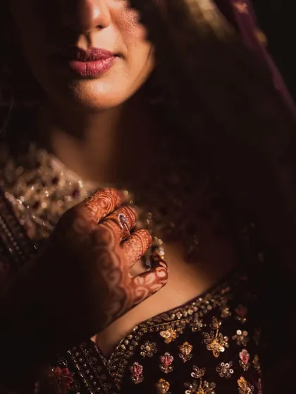 An artistic close-up focusing on the bride's lips and the intricate henna on her hand, capturing the sensual details of her look.