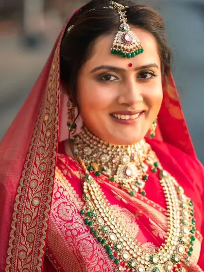 A close-up of the bride's smiling face. Her makeup is flawless, with a classic red bindi and lipstick that perfectly match her traditional attire.