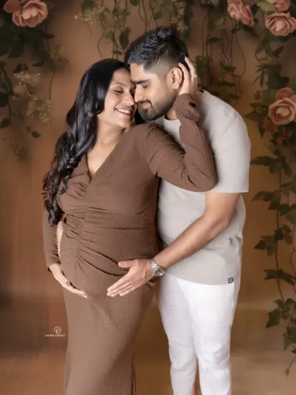 A warm and loving embrace between partners. The earthy tones and soft floral background create a romantic and natural feel for this beautiful couple's maternity portrait.