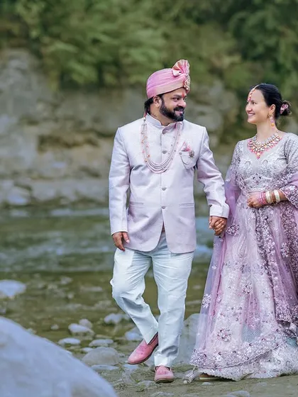 A royal walk by the riverside. The couple's elegant ethnic wear looks stunning against the rugged, natural backdrop of the river and green hills.