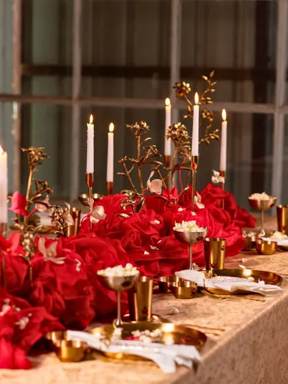 A 'Cascading Sindhoor' tablescape, where a dramatic red fabric centerpiece is paired with traditional Kansa tableware and golden floral sculptures for a contemporary Indian look.