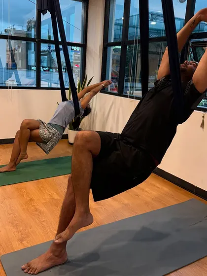 Two members relax in the hammocks, enjoying a moment of gentle stretching and release. Aerial yoga can be both an intense workout and a deeply restorative practice.