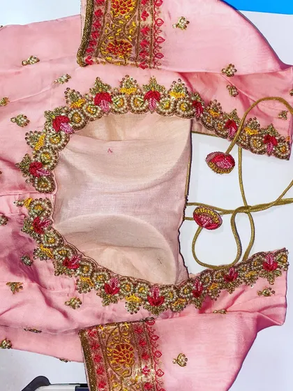 This pink blouse has a circular cutout back design. The border is decorated with multi-color floral embroidery and gold threadwork.