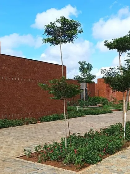 A paved walkway at the Bagchi Karunashraya hospice, lined with young trees and landscaping. The campus is designed to feel more like a garden retreat than a medical facility.