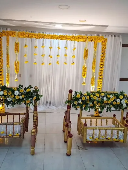 A simple and elegant floral decor for a twin baby girls' naming ceremony. We used two beautiful wooden cradles, a backdrop of white curtains with marigold garlands, and a peacock feather prop for a traditional touch.