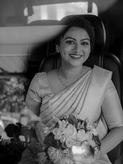 A classic black and white portrait of a bride holding her bouquet, smiling warmly. The monochrome adds a timeless quality.