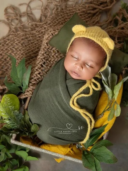 A cozy, wrapped baby in a basket. The earthy green and yellow tones and the simple, natural props create a feeling of warmth and comfort.