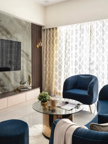 A view of the living room from the 'Royal Mansion' project, showing the interplay between the marble TV wall, dark wood fluting, and the rich blue velvet of the custom armchair and ottoman.