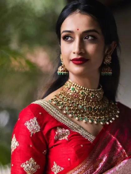 A close-up of the previous look. The focus is on the flawless skin, bold red lip, and the intricate details of the jewelry.