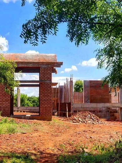 The "Elephants by the Lake" residence under construction, framed by trees. The design uses exposed brick and creates large openings to connect the inhabitants with the natural beauty of the site.