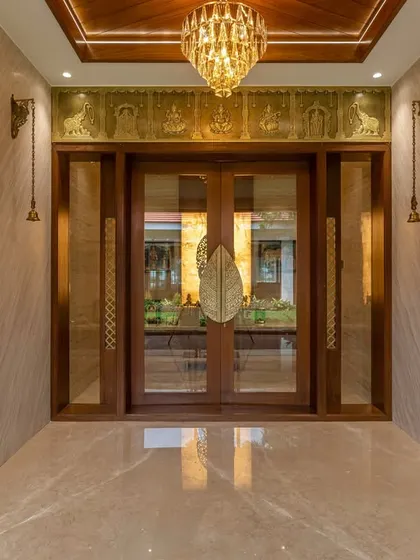 The entrance to the pooja room is framed with wood and features large glass doors with custom brass handles, making it a beautiful focal point in the home.