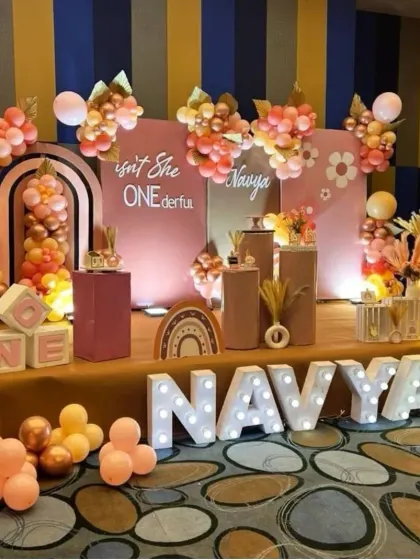 A trendy and warm boho-chic theme for a "ONEderful" first birthday. This decor features earthy tones of rose gold and terracotta, with light-up letters spelling the name "NAVYA" for a personalized focal point.
