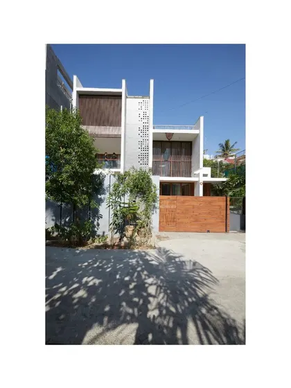 The facade of the Vikas Residence is a study in minimalism and texture. A perforated 'jaali' screen provides privacy and filters light, while a simple material palette of concrete, wood, and white plaster creates a calm and sophisticated exterior.
