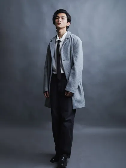 A full-length shot that showcases the complete outfit. The clean, simple studio background keeps the focus entirely on the model and his contemporary fashion look.