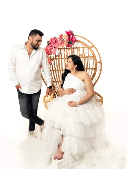 A regal and angelic maternity portrait. The mother-to-be seated on a peacock chair, dressed in a beautiful white gown, creates a stunning and timeless image of motherhood.