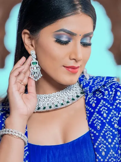 A modern take on bridal jewellery, this silver-finish choker with green stones is paired with a trendy blue jacket-style lehenga.
