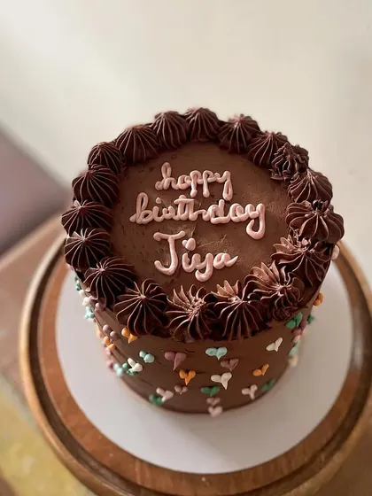 A tall chocolate cake that's as cute as it is delicious. The rich chocolate buttercream is covered in tiny, multi-colored piped hearts, making it a sweet and simple design for any birthday.