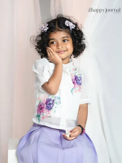 A sweet girl with curly hair and a floral shirt, her expression is shy and adorable. The soft studio lighting highlights her gentle features.