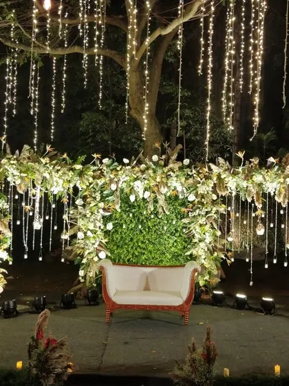 A romantic nighttime photo spot with a lush floral and foliage arch, illuminated by hanging fairy lights.
