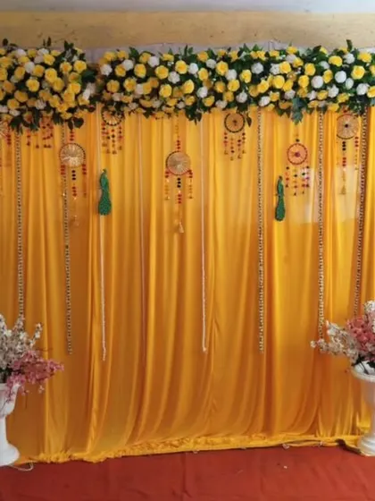 A simple and elegant backdrop for a home ceremony. We used a yellow fabric drape with hanging dreamcatchers and a floral border on top, flanked by two white pedestals with flower pots.