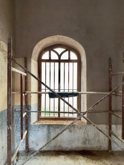 A newly restored arched window, still surrounded by scaffolding. The clean lines of the new plaster and the repaired window frame contrast with the raw state of the surrounding walls, showing the project in transition.