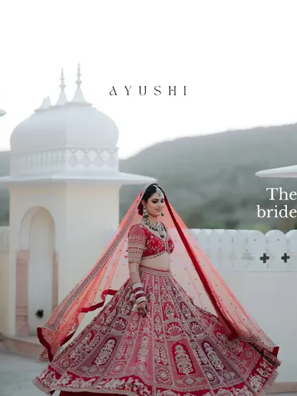 A majestic portrait of the bride, her red lehenga spread out, with the beautiful architecture of the venue creating a regal and expansive backdrop.